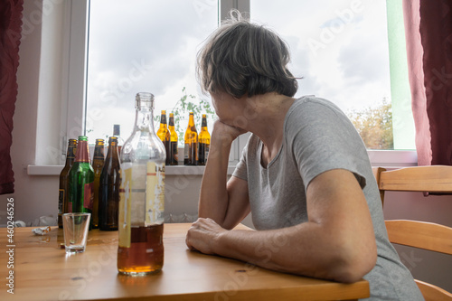 old senior female woman sit next to table drink alcohol bottle at home sad alone alcoholism Signs and Symptoms rehab abuse and recovery problems