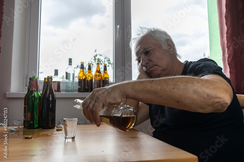 old senior male man sit next to table drink alcohol bottle at home sad alone alcoholism Signs and Symptoms rehab abuse and recovery problems photo