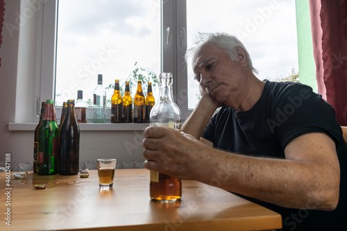 old senior male man sit next to table drink alcohol bottle at home sad alone alcoholism Signs and Symptoms rehab abuse and recovery problems