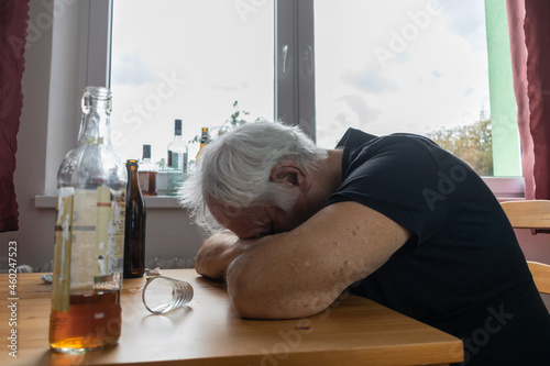 old senior male man sit next to table drink alcohol bottle at home sad alone alcoholism Signs and Symptoms rehab abuse and recovery problems