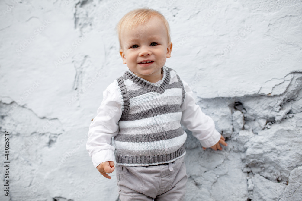Fototapeta premium Stylish male toddler dressed fashion clothes, grey jeans, sweater and walking against the street wall