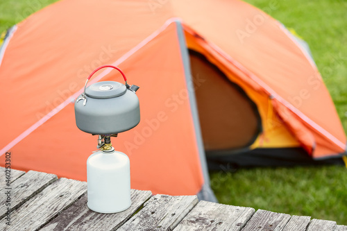 kettle on a gas burner with orange tent in a camping site. The stove is used for more eco-friendly and safe cooking instead of kindling a fire