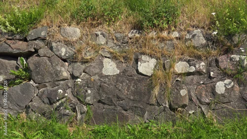 A view of an ancient stone-made wall merged with the hill, having grass-grown into it. A view of an ancient stone-made wall merged with the hill, having grass-grown into it.