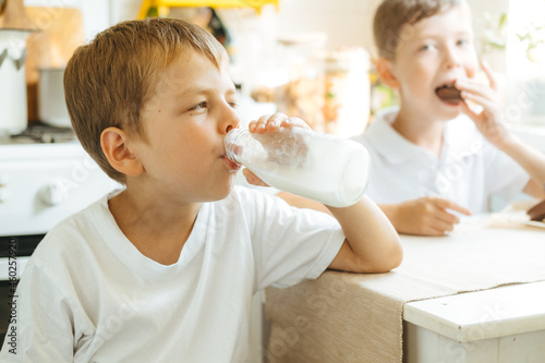 Фотография A boy is drinking milk from a bottle in the kitchen at home