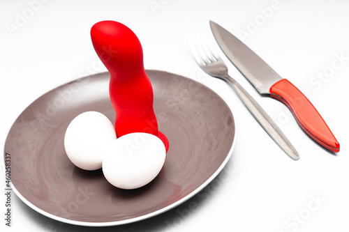 there is a dildo on the plate, and next to it a knife and fork, as well as 2 eggs - a symbol of a male organ; a grotesque on the theme of nymphomania or feminism