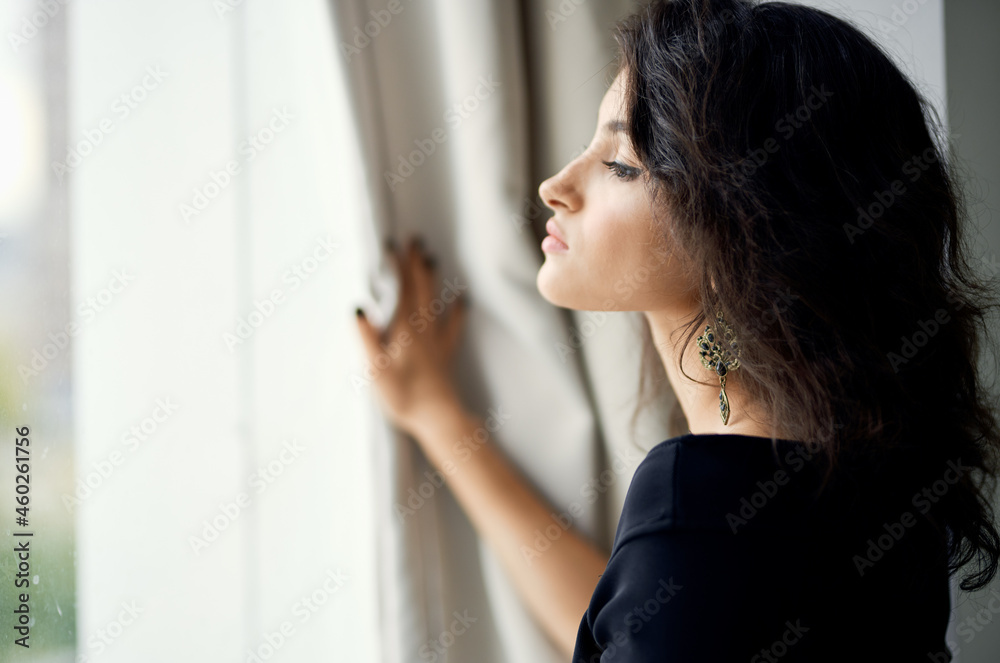 Woman in black dress near the window fashionable hairstyle decoration luxury Woman in black dress near the window fashionable hairstyle decoration luxury
