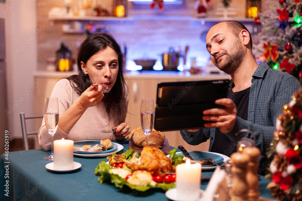 Joyful couple eating delicious dinner sitting at table in xmas decorated kitchen celebrating christmas holiday. Family watching entertainment movie enjoying winter time together. Santa-claus season Joyful couple eating delicious dinner sitting at table in xmas decorated kitchen celebrating christmas holiday. Family watching entertainment movie enjoying winter time together. Santa-claus season