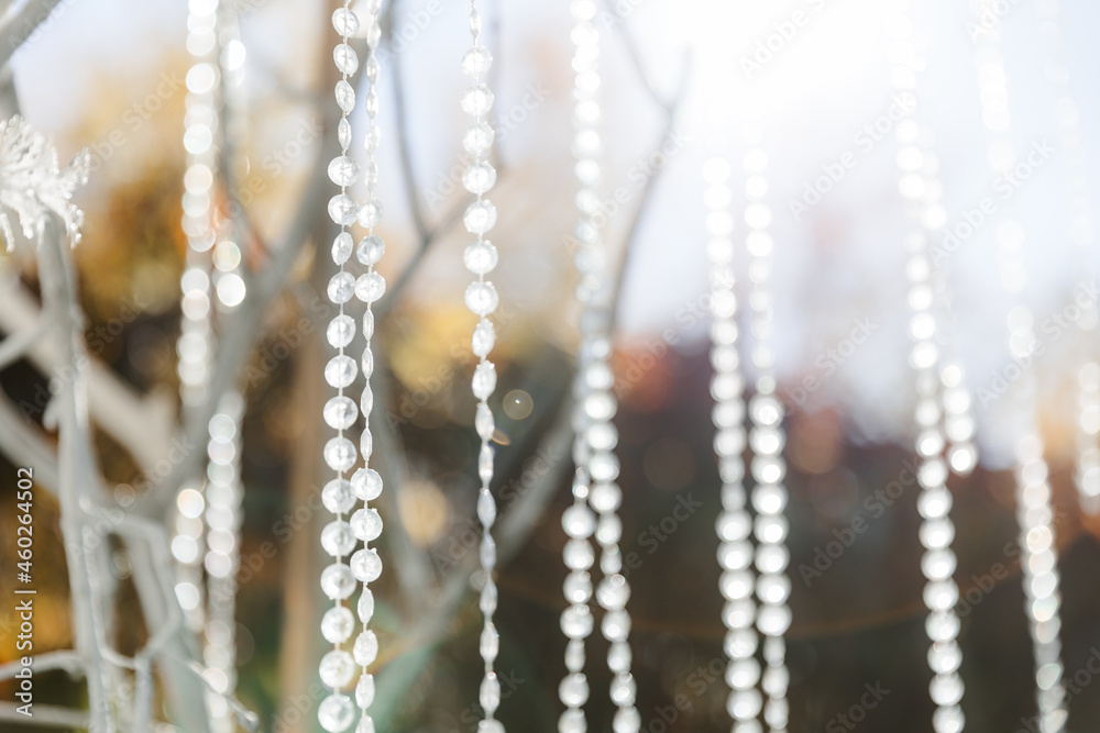 Glass, plastic, transparent beads in the form of crystals hang as decorations on the holiday close-up. White decor. Wedding ceremony on the street on the green lawn. Glass, plastic, transparent beads in the form of crystals hang as decorations on the holiday close-up. White decor. Wedding ceremony on the street on the green lawn.