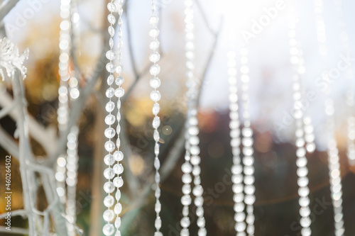 Glass, plastic, transparent beads in the form of crystals hang as decorations on the holiday close-up. White decor. Wedding ceremony on the street on the green lawn.