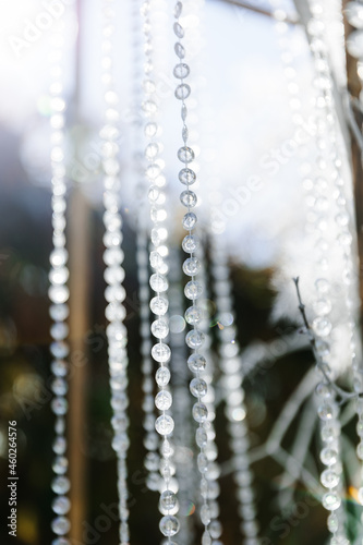 Glass, plastic, transparent beads in the form of crystals hang as decorations on the holiday close-up. White decor. Wedding ceremony on the street on the green lawn.