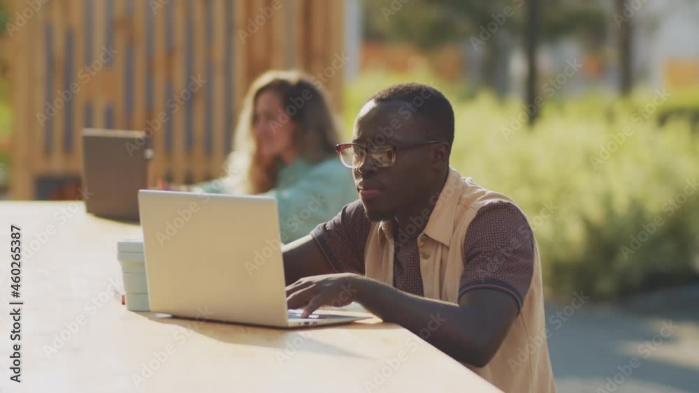 Young African American freelancer working on laptop at table in park on summer day Young African American freelancer working on laptop at table in park on summer day