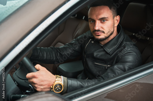 Portrait of handsome young man driving modern car. Guy driver wearing casual clothes and gold watch. © anatoliy_gleb