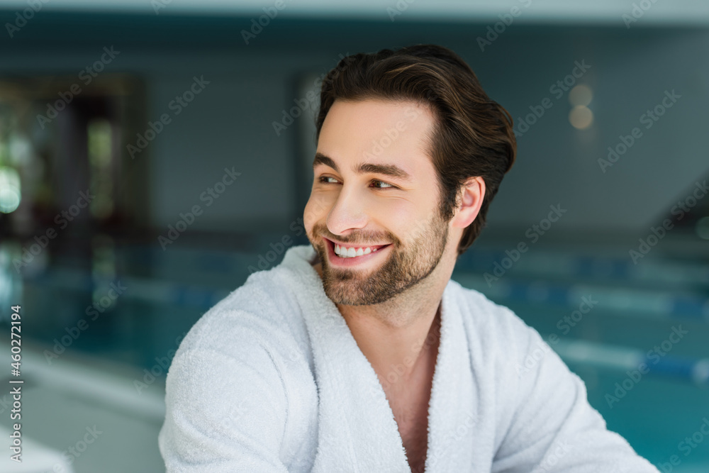 Cheerful man in white bathrobe looking away in spa center