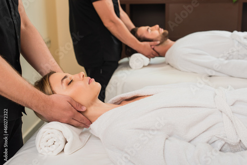 Masseur doing neck massage to young woman in bathrobe near colleague and man in spa center