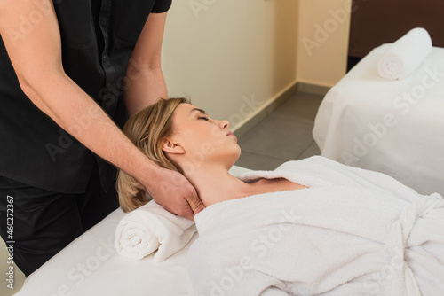 Masseur doing neck massage to woman in bathrobe