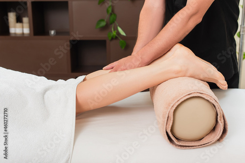 Cropped view of masseur doing massage on leg of young woman in spa center