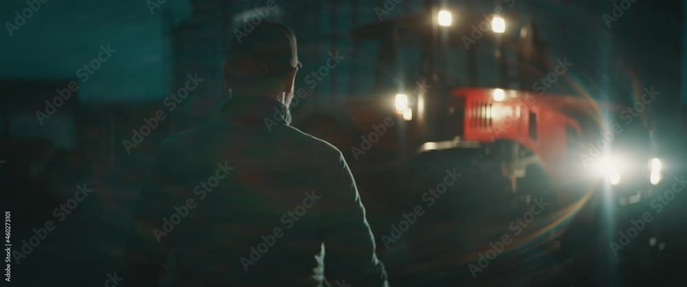 Caucasian farmer walking towards tractor at dawn early in the morning before sunrise. Shot with 2x anamorphic lens