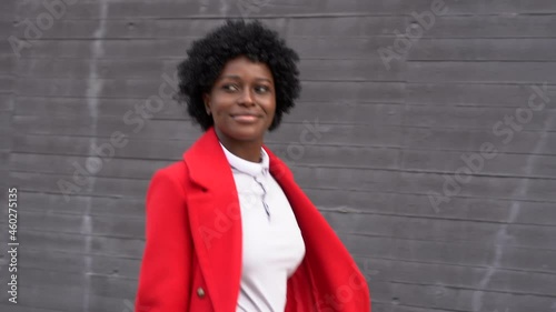 Stylish Afro woman looks away and smiles while walking down the street. Urban concept.