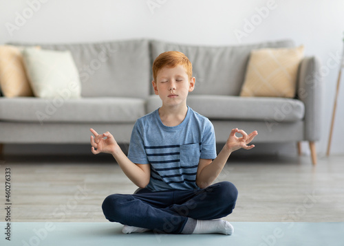 Relaxed boy sitting on fitness mat at home, meditating