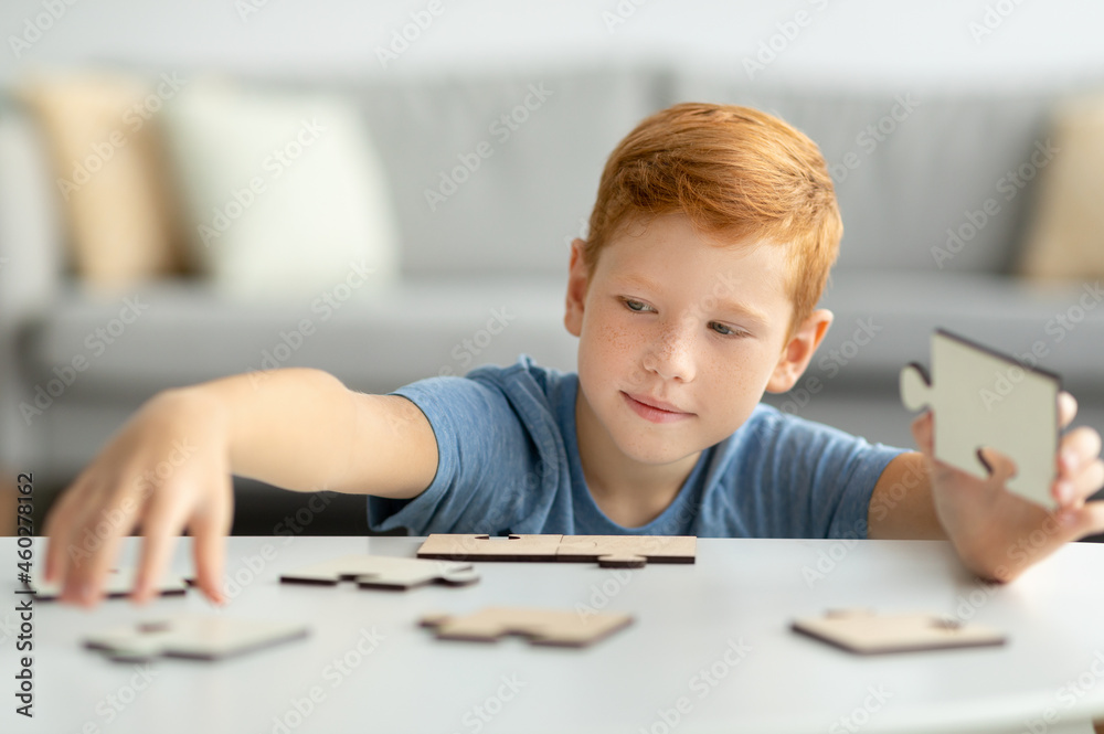 Smart redhead boy holding wooden puzzles, playing alone at home Smart redhead boy holding wooden puzzles, playing alone at home