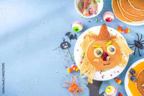 Creative homemade Halloween pancakes for breakfast, in form of funny monsters, ghost, bat, witch. With traditional trick or treat sweets, candy and decorations, top view on colorful blue background © ricka_kinamoto