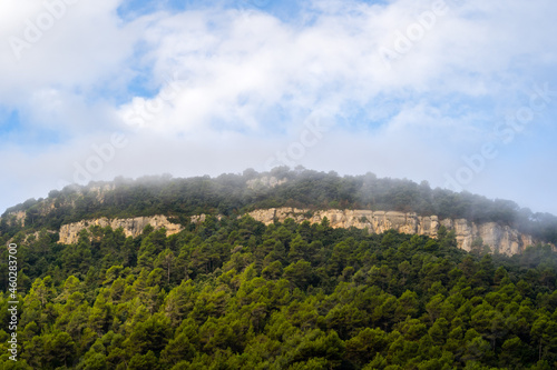 mountain with green forest and rock wall with clouds surrounding it catalonia, spain