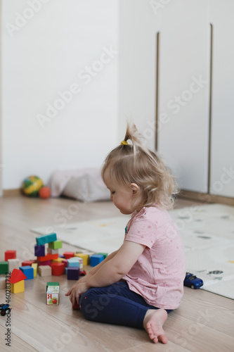 a little funny girl plays with cubes and toys on the floor in the nursery