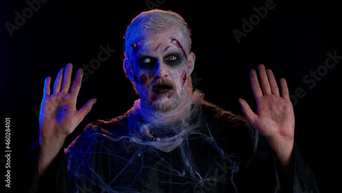 Surrender. Sinister man in costume of Halloween crazy zombie with bloody wounded scars face scared by police lights isolated on black room. Horror theme of cosplay wounded undead, beast, monster