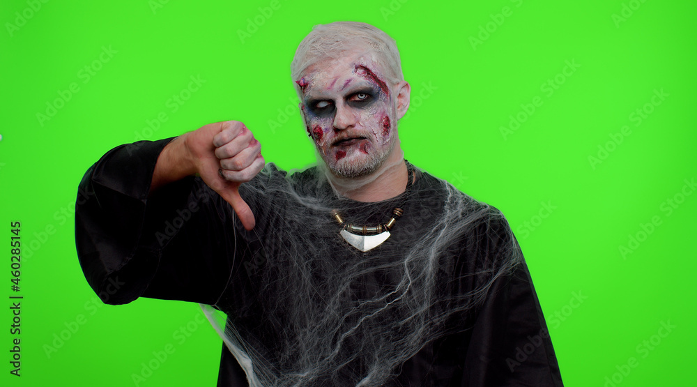 Sinister man in carnival costume of Halloween crazy zombie with bloody wounded scars face showing thumbs down sign gesture, expressing discontent, disapproval, dissatisfied, dislike. Cosplay undead Sinister man in carnival costume of Halloween crazy zombie with bloody wounded scars face showing thumbs down sign gesture, expressing discontent, disapproval, dissatisfied, dislike. Cosplay undead