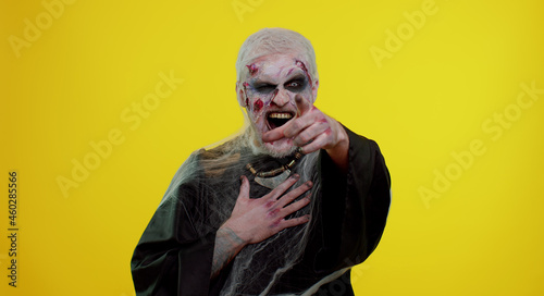 Sinister man in carnival costume of Halloween crazy zombie with bloody wounded scars face pointing finger to camera, laughing out loud, taunting making fun of ridiculous appearance, funny joke. Horror