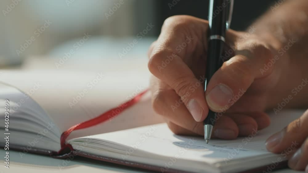 Horizontal close-up shot footage of unrecognizable mans hand holding pen writing something in notebook