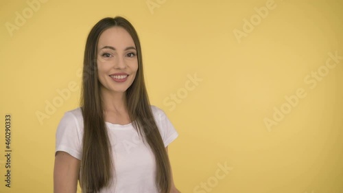 Attractive smiling woman 35 years old in a white basic t-shirt on a yellow background. Shows the offer on the palm.