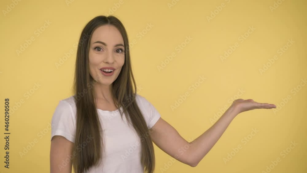 Attractive smiling woman 35 years old in a white basic t-shirt on a yellow background. Shows the offer on the palm. Attractive smiling woman 35 years old in a white basic t-shirt on a yellow background. Shows the offer on the palm.