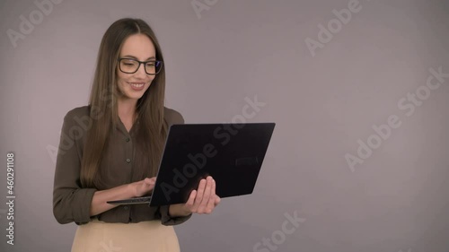 Attractive serious business woman 30 years old in a dark green office shirt. Woman working on a laptop while standing on a gray background.