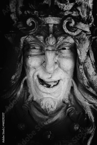 Monster face of aGreek antique god daimon of eager rivalry  envy  jealousy  and zeal Zelus  Zelos . Fragment of an ancient stone statue. Vertical image.