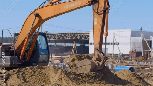 Earthwork at a construction, excavator scoop flattens large mountains of sand 