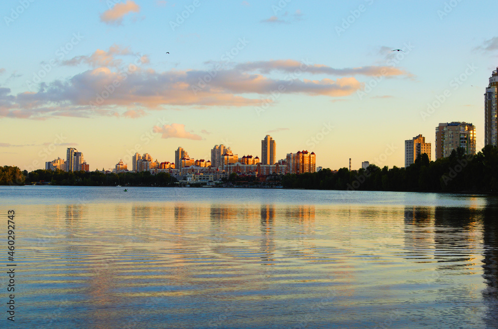 Amazing autumn landscape during sunset. Buildings reflected in the tranquil water of the Dnieper River. High rise buildings of the Obolon neighborhood in the background
