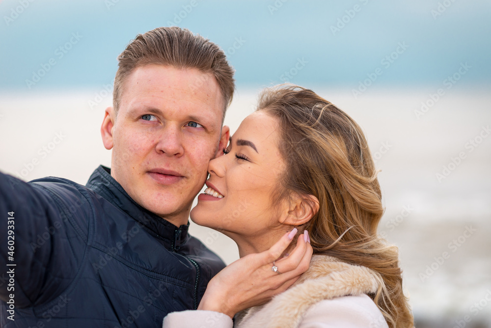 Beautiful young happy woman hugging cuddle young boyfriend while taking selfie photo on sunny autumn beach.Close up. Beautiful young happy woman hugging cuddle young boyfriend while taking selfie photo on sunny autumn beach.Close up.