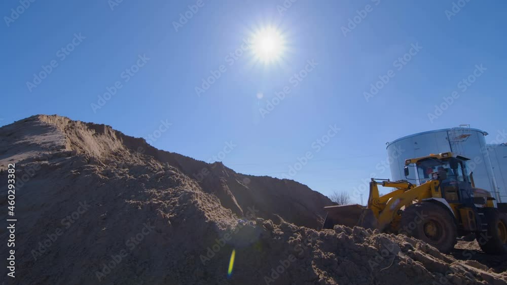Wheel loader, with its large bucket in front, moves large amounts of land and creates large mountain at the construction site Wheel loader, with its large bucket in front, moves large amounts of land and creates large mountain at the construction site