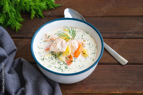 Salmon soup with cream, potatoes, carrots and herbs in a bowl on a dark wooden background. Lohikeitto soup. Copy space. photo