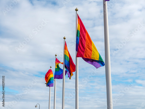 A row of flagpoles with gay pride flags blowing in the wind.