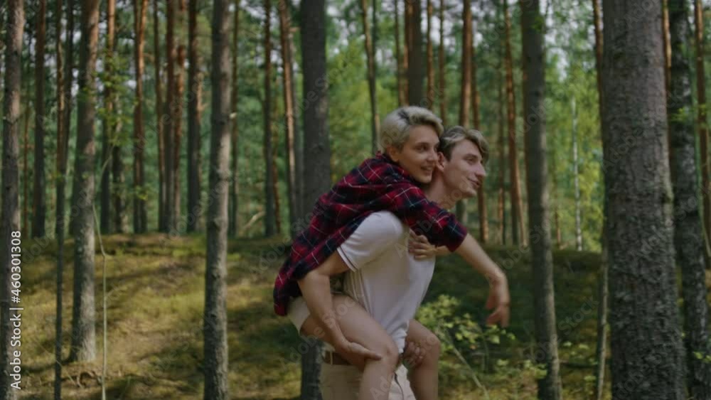 Young millennial couple spend time in nature, walk in green summer forest. Man carry woman in his arms. Piggy back ride of couple in love on outdoors date Young millennial couple spend time in nature, walk in green summer forest. Man carry woman in his arms. Piggy back ride of couple in love on outdoors date