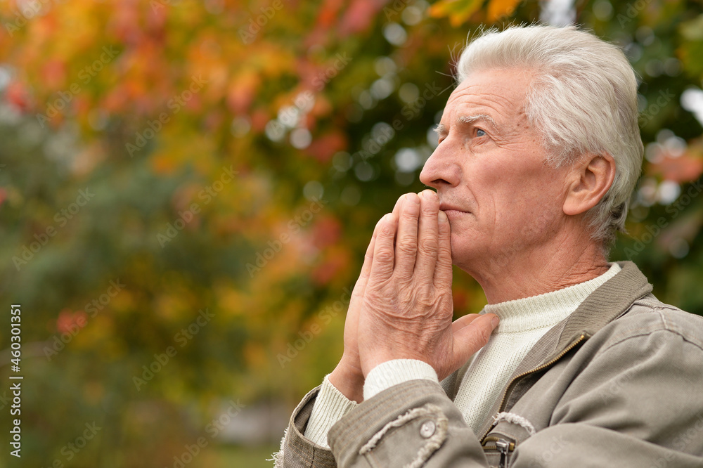 Portrait of a thoughtful senior man praying in autumn park Portrait of a thoughtful senior man praying in autumn park