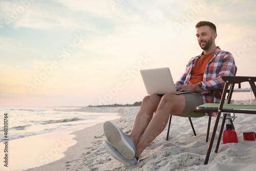 Man using laptop in camping chair on sandy beach