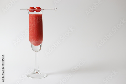 Long glass with fresh red tomato juice with metal stick with two candy tomatoes on white background.