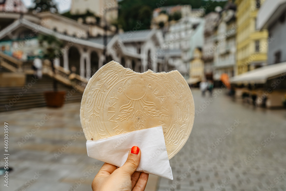 Famous Carlsbad wafer,CZ: lazenske oplatky, originated in 1867. Woman hand holding traditional Czech sweet cookie snack made in Karlovy Vary, famous spa city on UNESCO list.Tasty food background