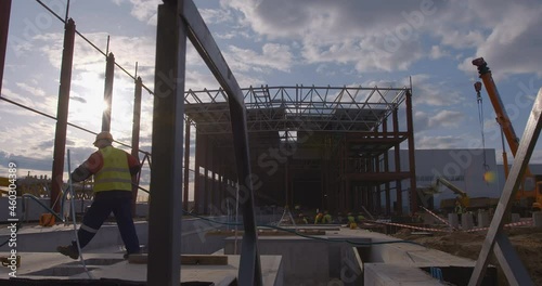 At construction site, a worker pulls a powerful electrical cable against the background of a factory workshop under construction