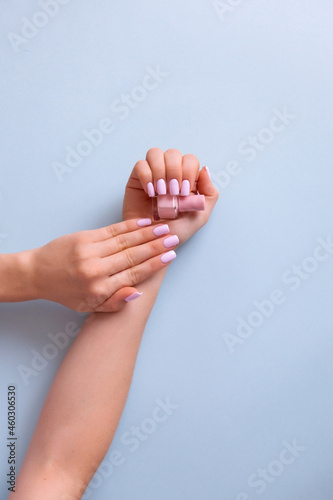 Stylish trendy female manicure. Beautiful young woman's hand with perfect pink manicure on blue background.