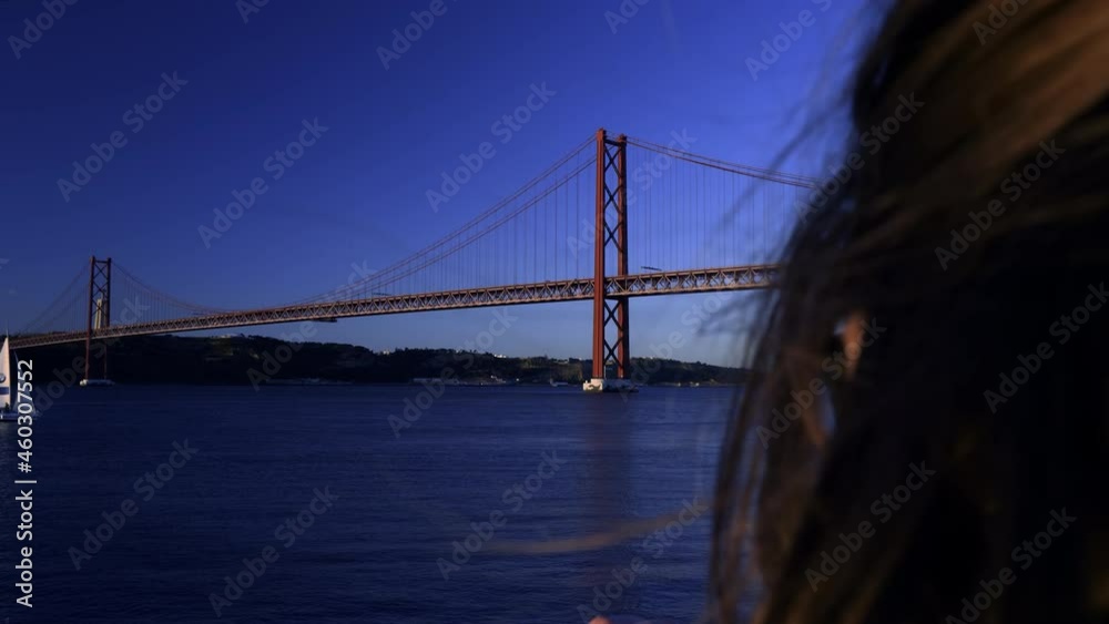 Woman taking photo on her smartpohne of the Ponte 25 de Abril bridge over the Tejo river in Lisbon at dusk - beautiful blue colors and calm waters Woman taking photo on her smartpohne of the Ponte 25 de Abril bridge over the Tejo river in Lisbon at dusk - beautiful blue colors and calm waters