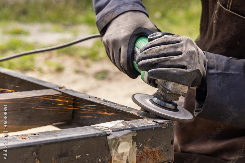 A close up shot of a welder hands, wearing gray protective gloves, holding a welding machine, running on a metal surface, fire sparks spread around A close up shot of a welder hands, wearing gray protective gloves, holding a welding machine, running on a metal surface, fire sparks spread around